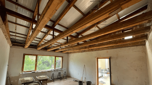 Blick in einen Rohbau mit sichtbaren Deckenbalken und Baustellenmaterialien