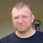Porträt eines Mannes mit Brille vor einer Baustellenwand