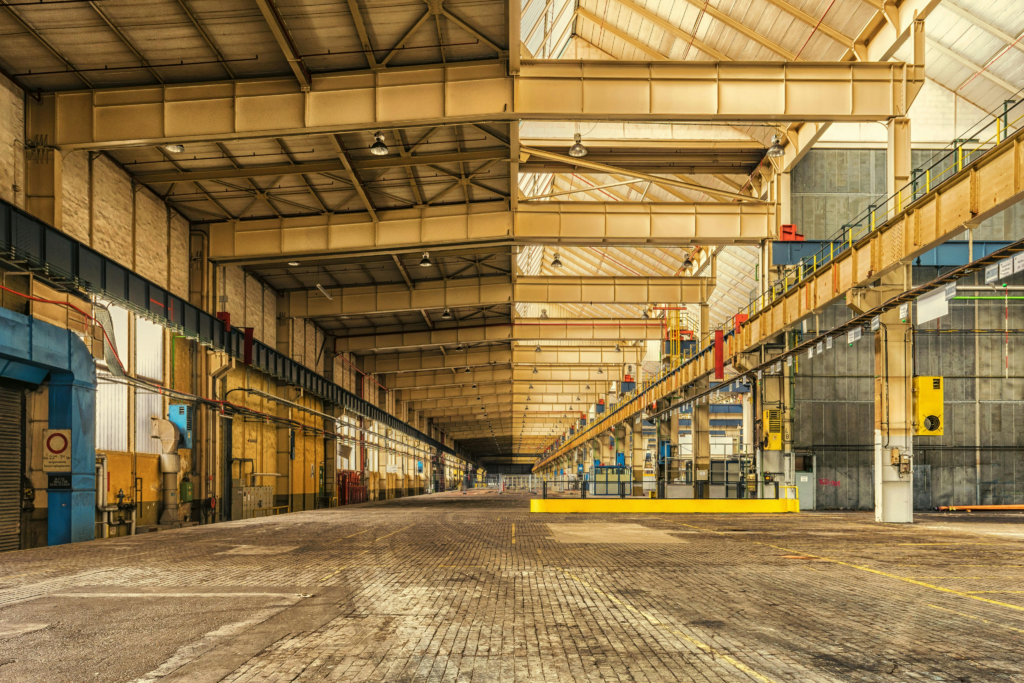 Große leere Industriehalle mit Stahlträgern und Betonboden unter hellem Dach