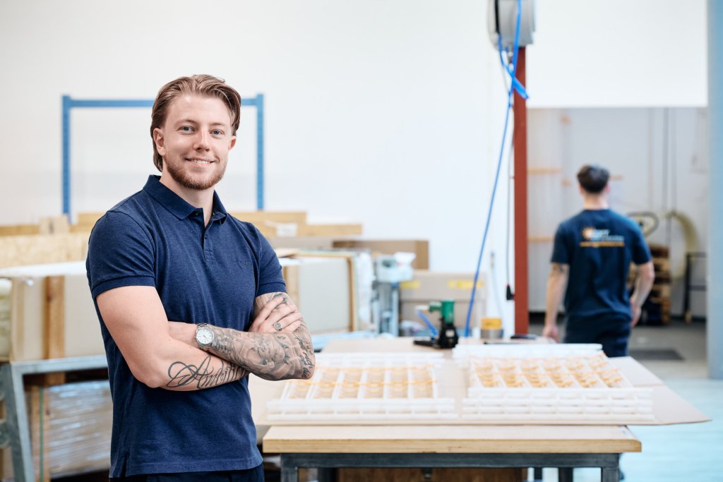 Mann mit Tattoos steht in Werkstatt vor Tisch mit Kunststoff-Registern für Flächenheizung