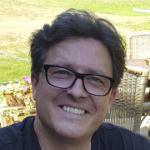 Porträt eines lächelnden Mannes mit Brille im Freien vor Gartenmöbeln