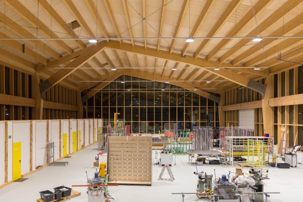 Große Werkhalle mit Holzdecke und verschiedenen Arbeitsstationen und Geräten