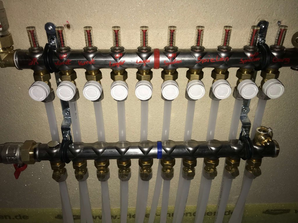 Rohrverteiler mit mehreren Ventilen und angeschlossenen weißen Schläuchen an der Wand