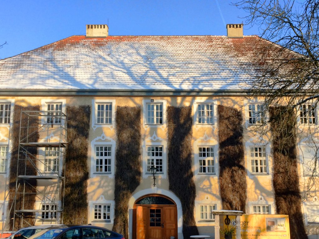Historisches Gebäude mit verschneitem Dach und Schatten von Bäumen an der Fassade