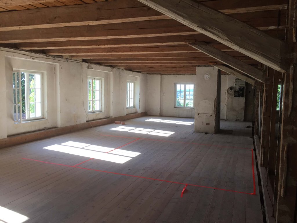 Helles, leeres Zimmer mit Holzbalkendecke und großen Fenstern