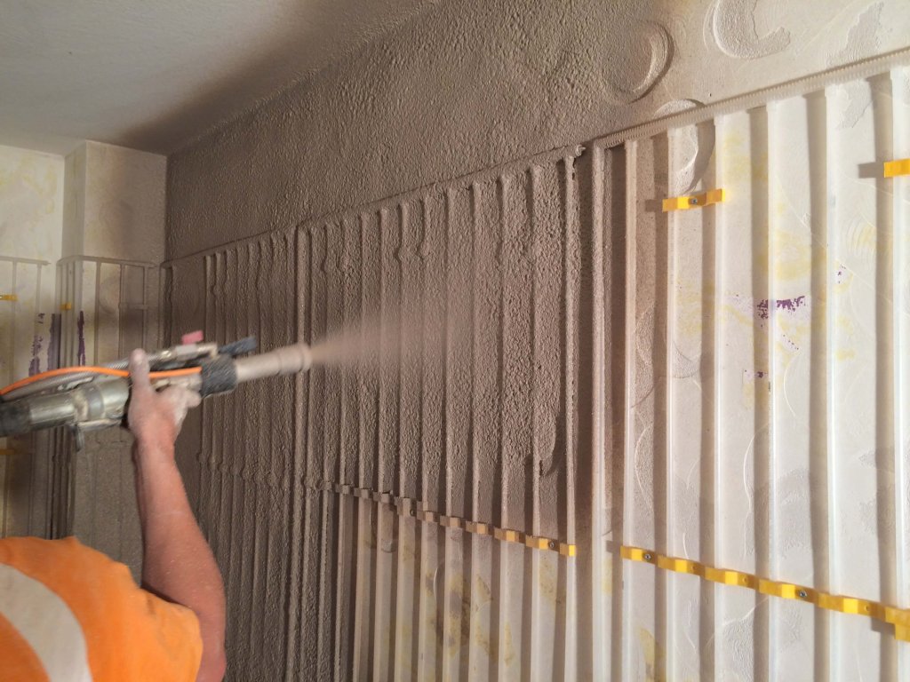 Person sprüht Dämmmaterial auf Wand für bessere Klimatisierung