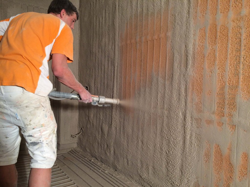 Mann sprüht Dämmmaterial auf Wand im Innenraum für Egger Klima