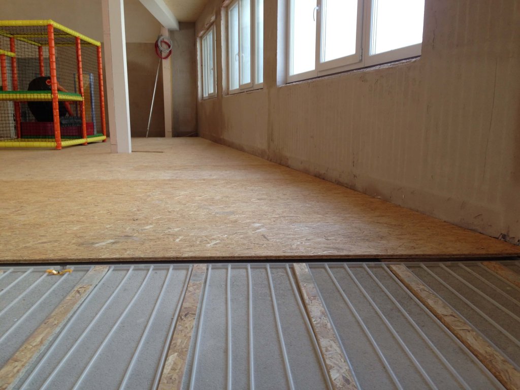 Bodenheizung unter Holzboden in einem Raum mit großen Fenstern und Spielbereich