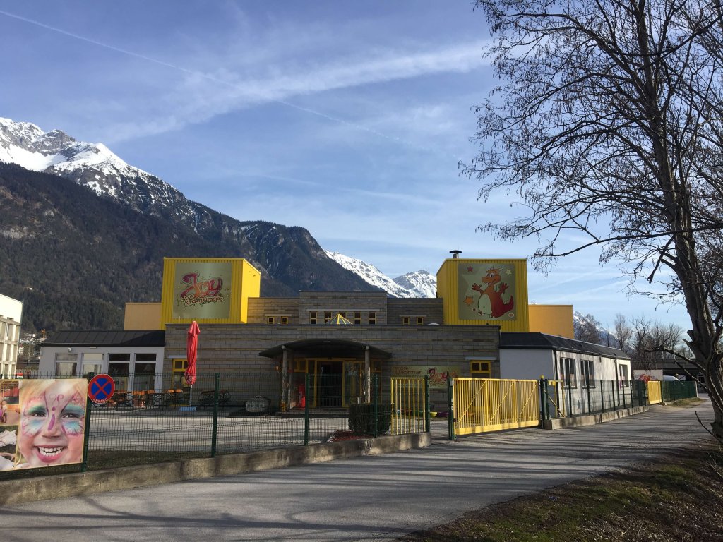 Gebäude mit gelben Aufbauten vor schneebedeckten Bergen und blauem Himmel