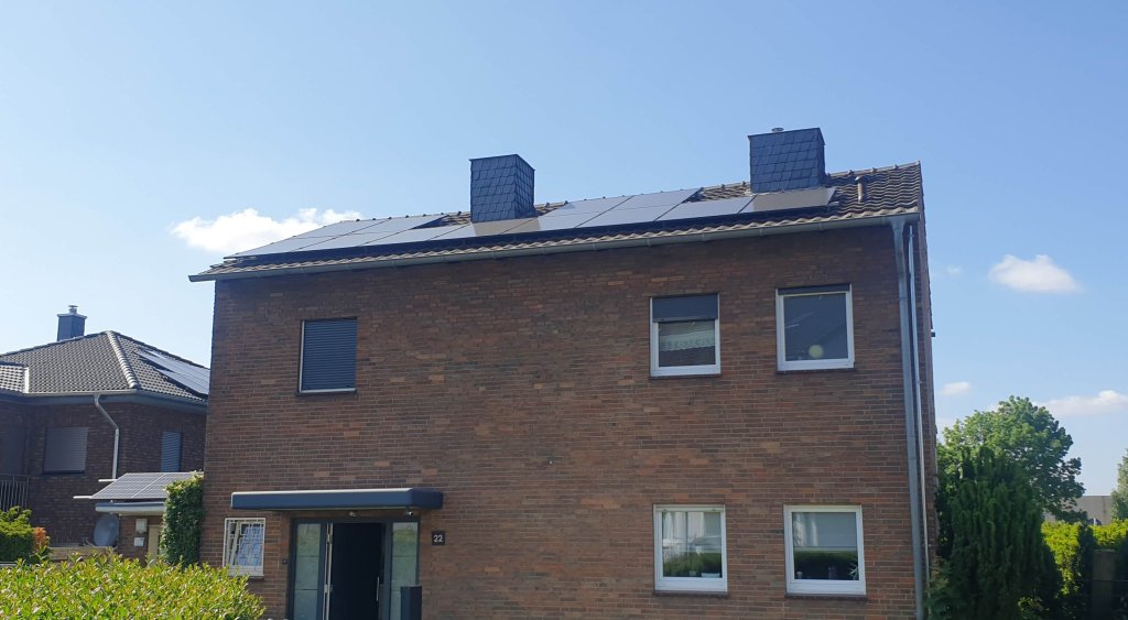 Zweistöckiges Backsteinhaus mit Solarpaneelen auf dem Dach bei klarem Himmel