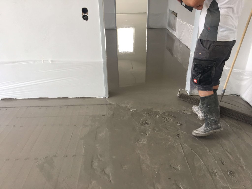 Handwerker trägt nasse Bodenbeschichtung in Innenraum auf