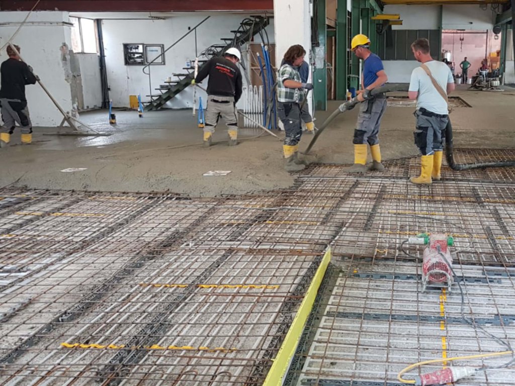 Arbeiter verteilen Beton auf Baustelle mit Stahlmatten im Vordergrund