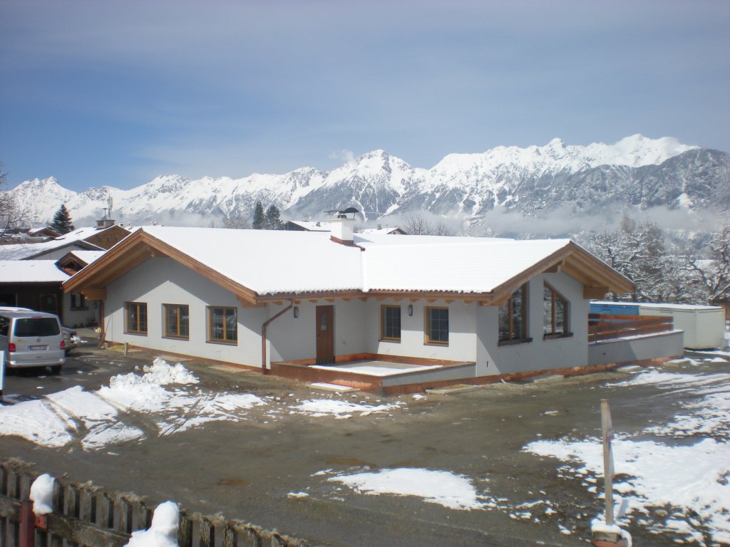 Einfamilienhaus mit Schnee bedeckt vor verschneiten Bergen und blauem Himmel