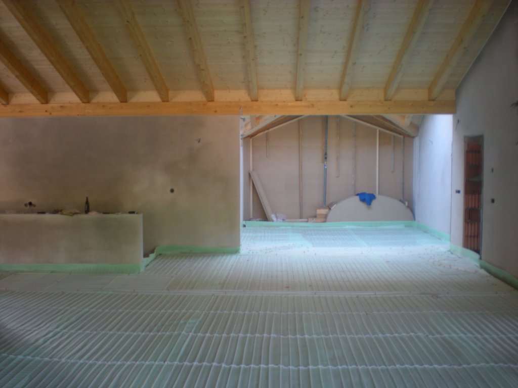 Innenraum mit sichtbaren Holzbalken und Boden mit Dämmplatten für Fußbodenheizung