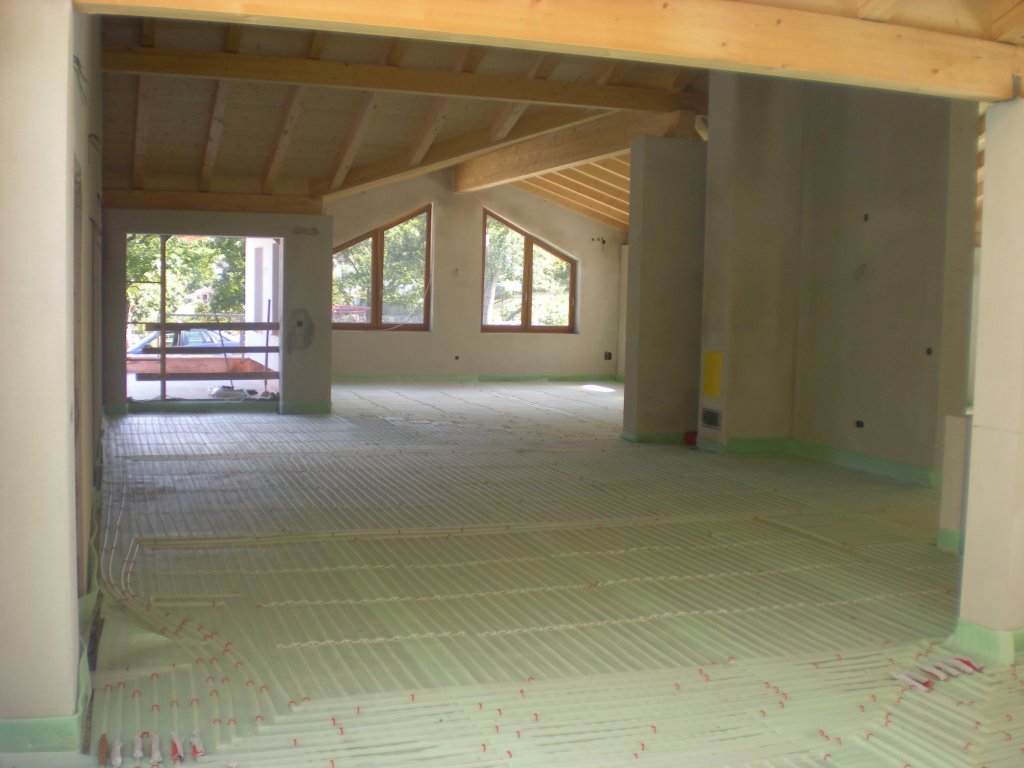 Großer heller Raum im Rohbau mit sichtbaren Holzbalken und Fußbodenheizung