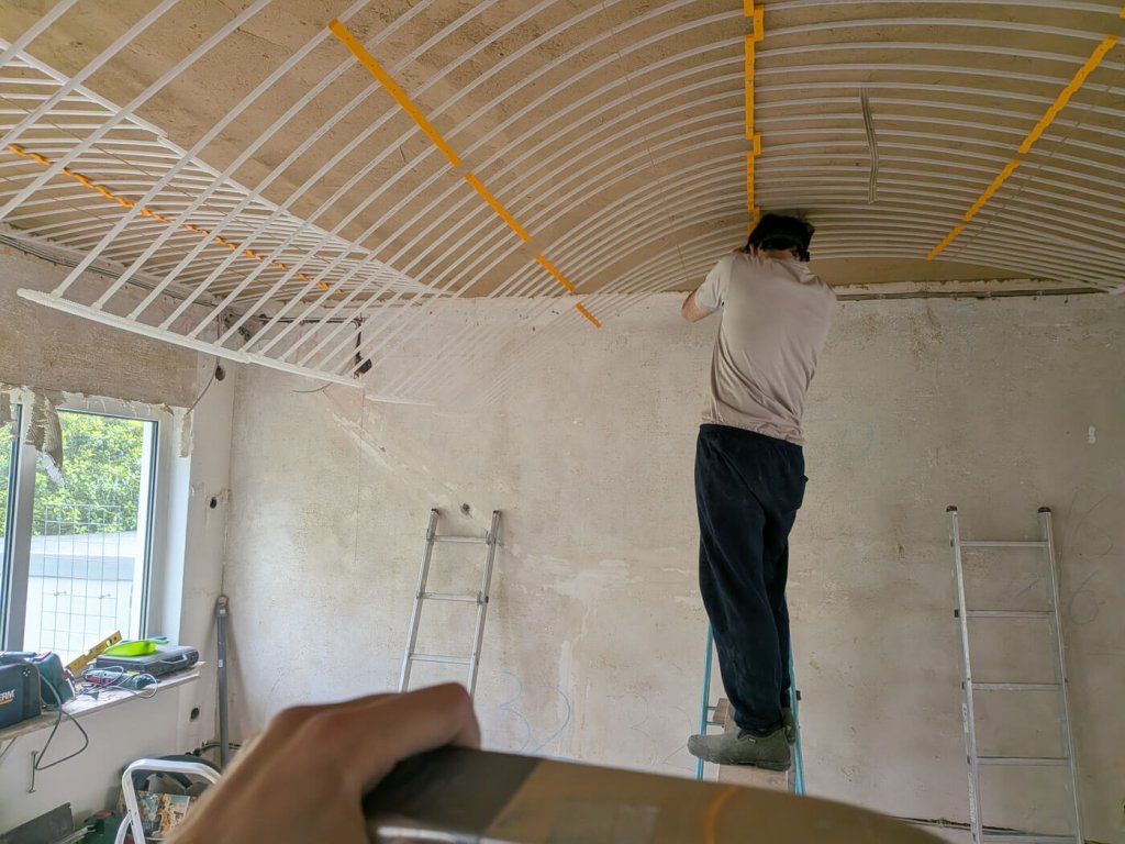 Person montiert Deckeninstallation in einem Raum mit Leitern und Werkzeug